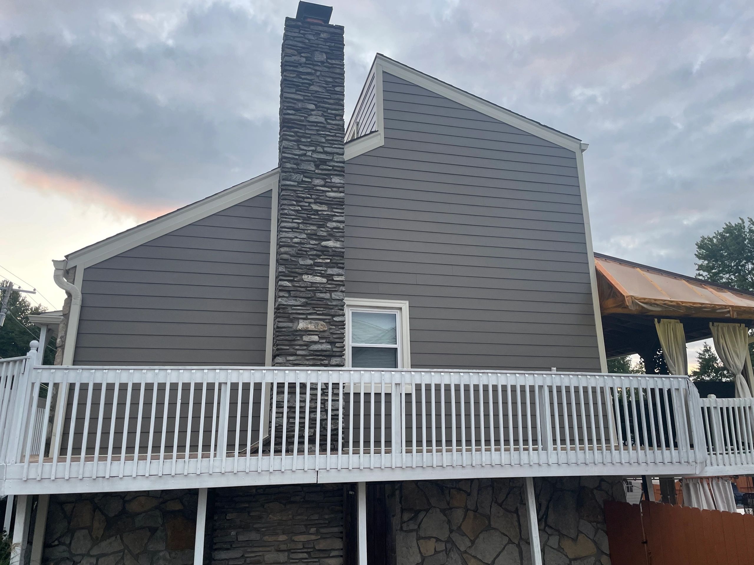 Modern residential house with gray horizontal siding and stone chimney